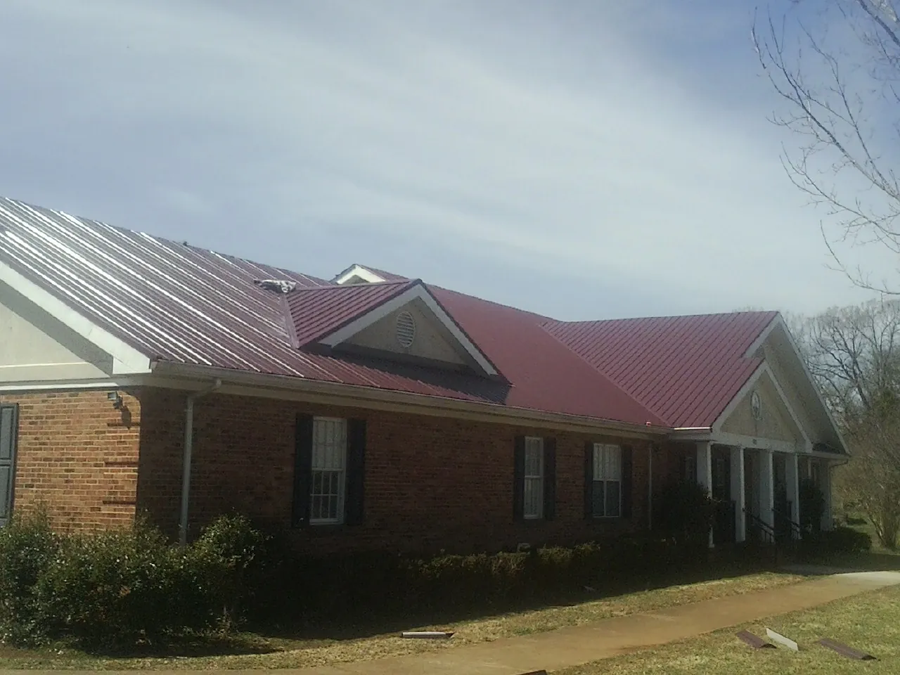 Red metal roof with gabled entries on a long brick building, from a Hail Damage Roof Repair job in Canoga Park