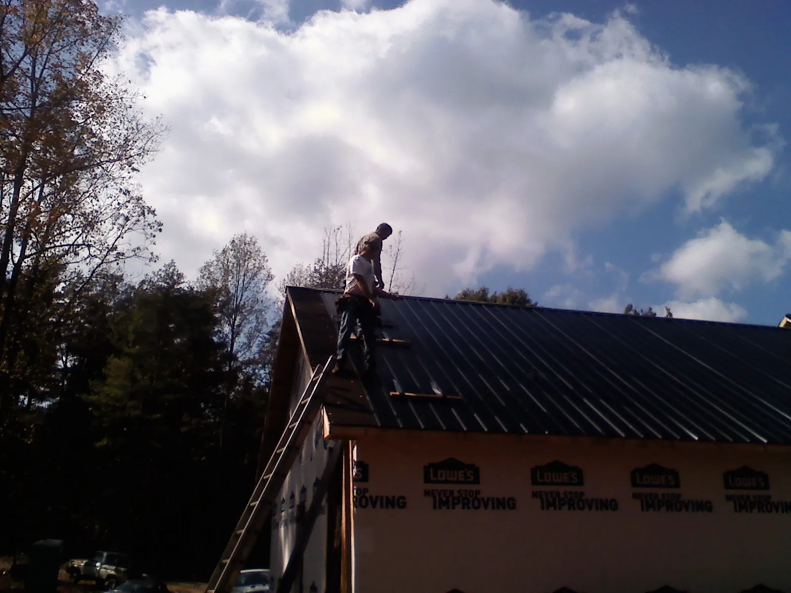 Roofer fastening dark metal panels high against a cloudy sky, from a Roof Inspection job in Canoga Park