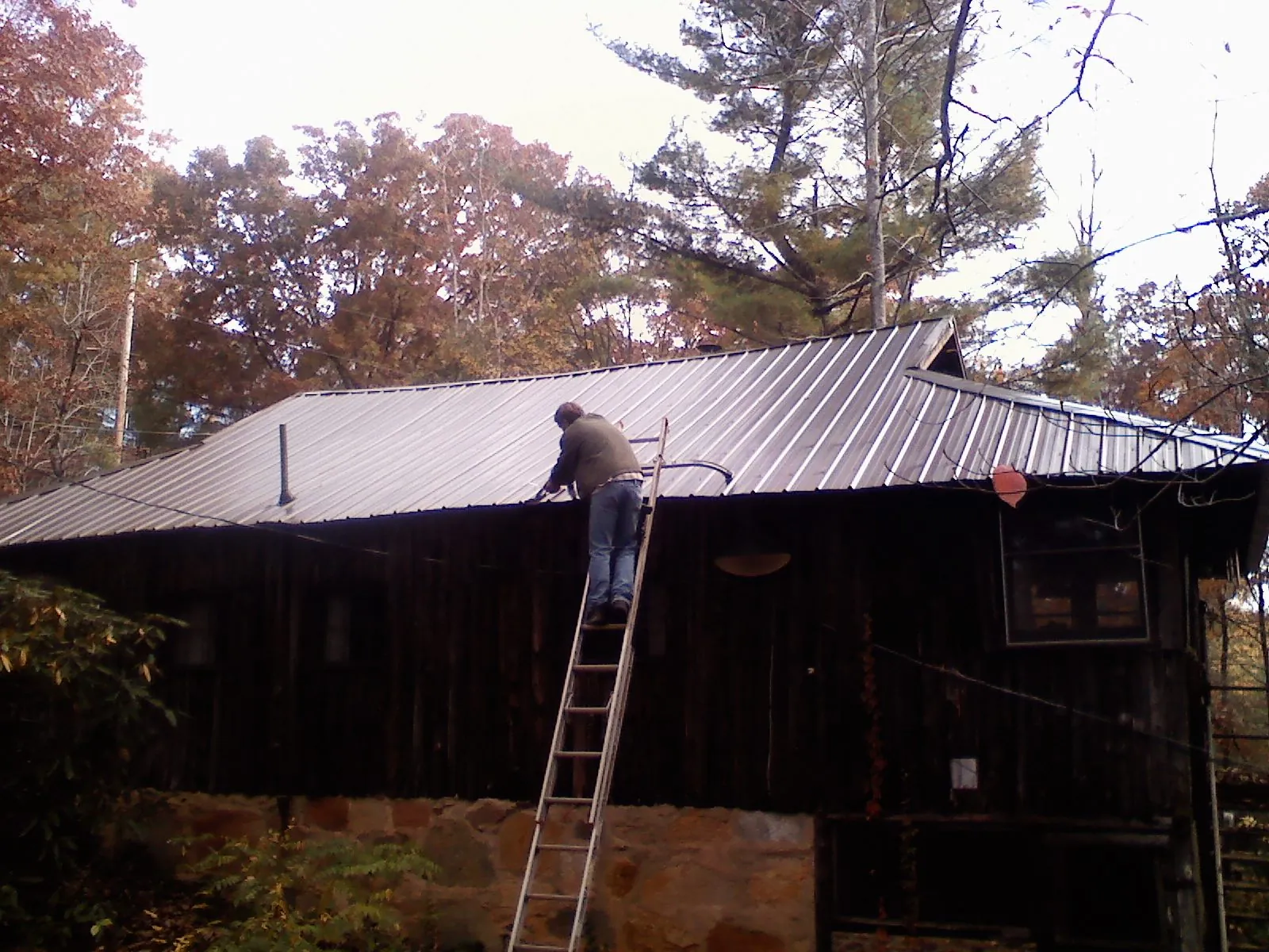 Roofer on a ladder working along the edge of a cabin metal roof in Canoga Park