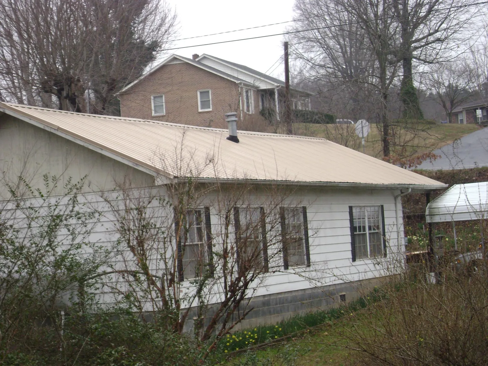 Tan metal roof on a white sided house set into a hillside — Commercial Roofing by Roofing Brothers in Canoga Park